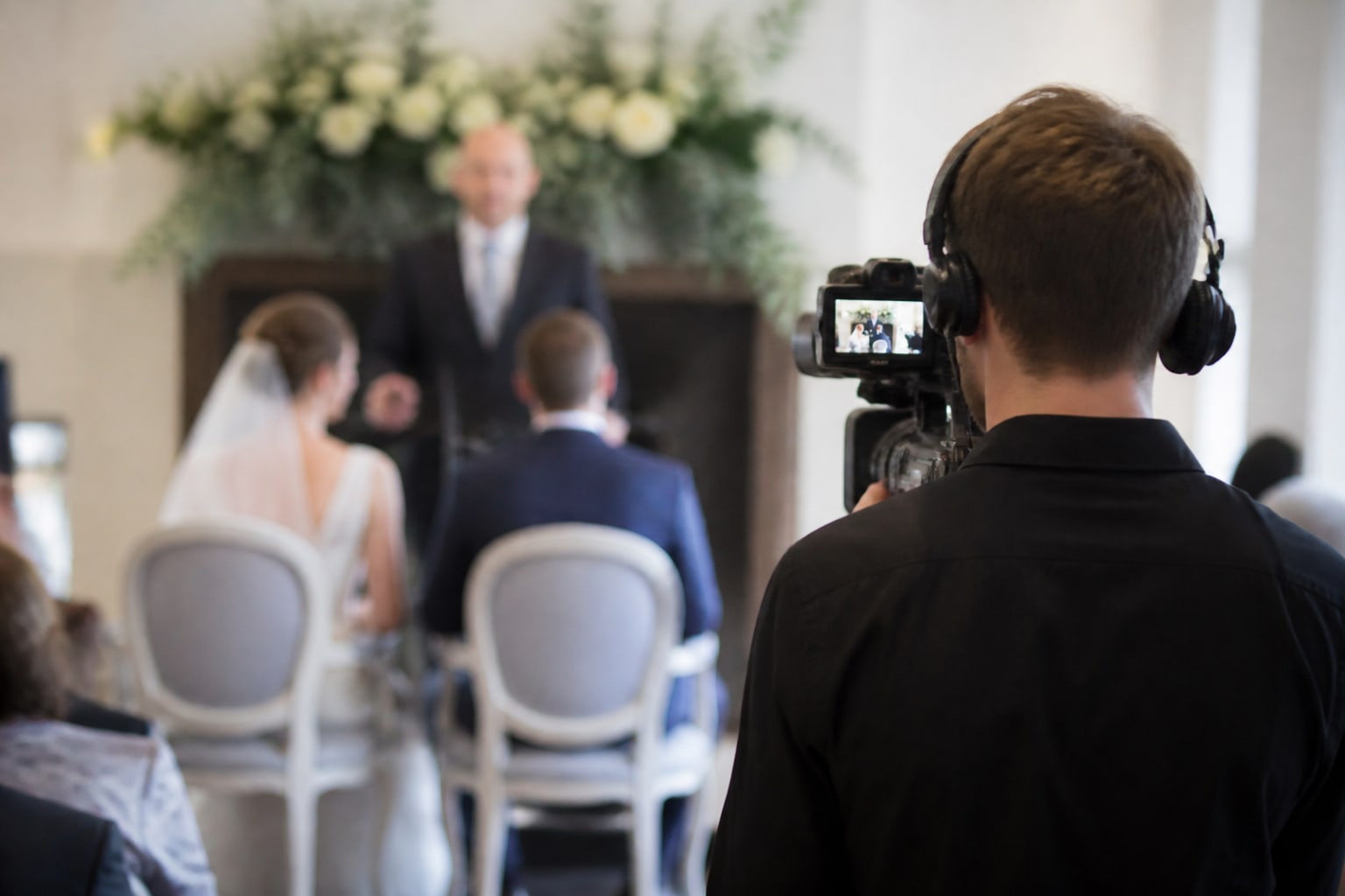 Een videograaf met koptelefoon filmt de ceremonie van achter de gasten