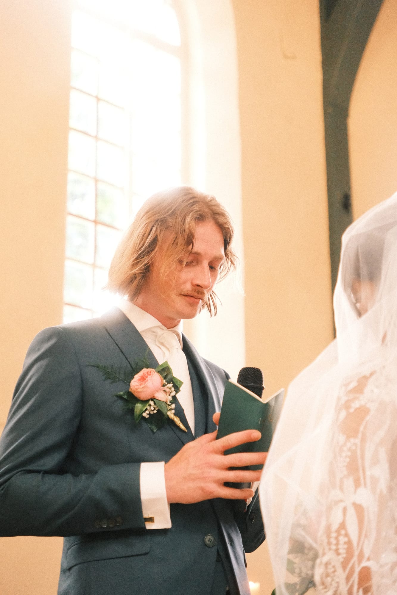 De bruidegom leest voor uit een boekje tijdens de ceremonie, de bruid met sluier naast hem