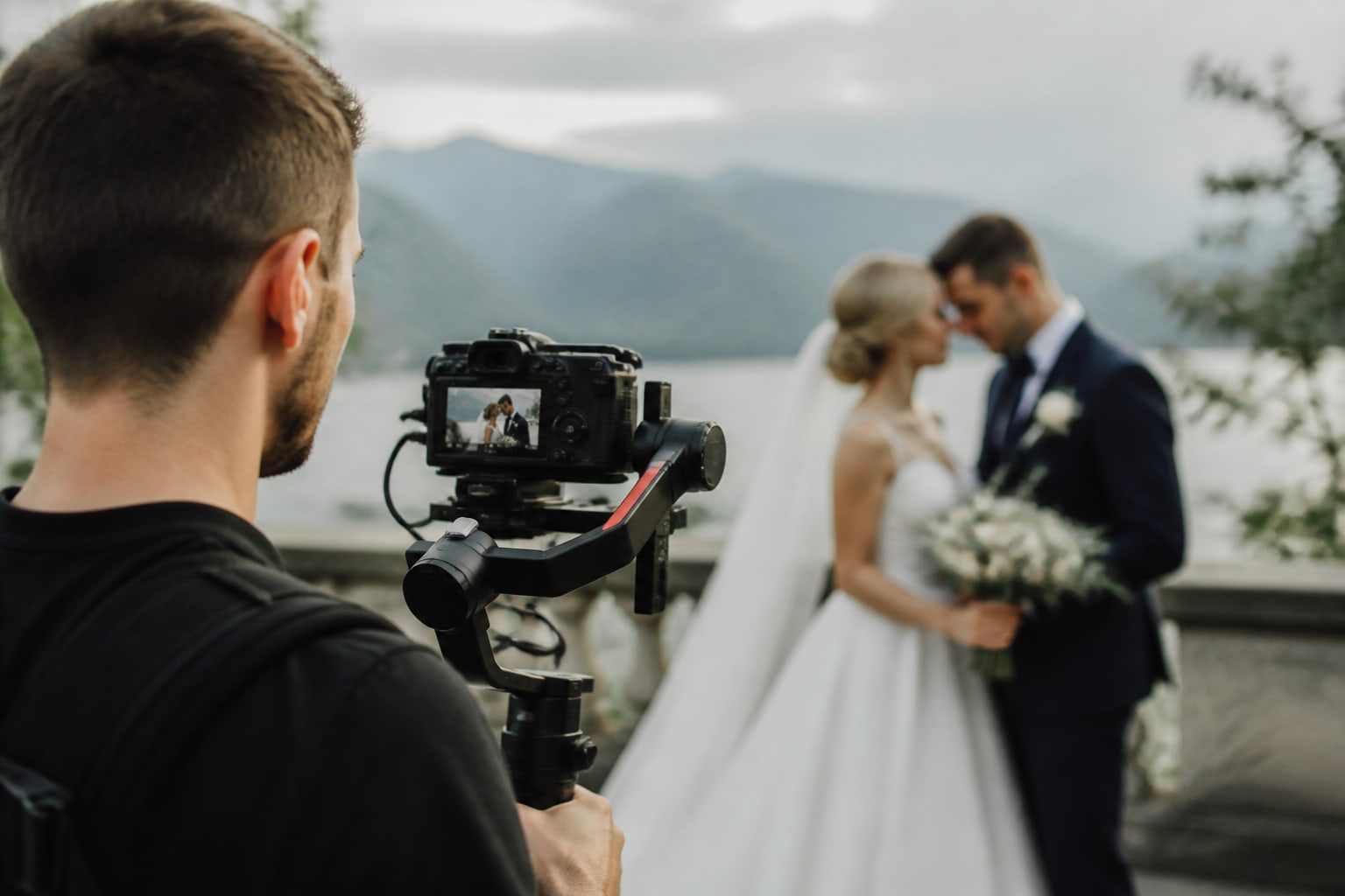 Een videograaf filmt het bruidspaar op een terras, met bergen op de achtergrond