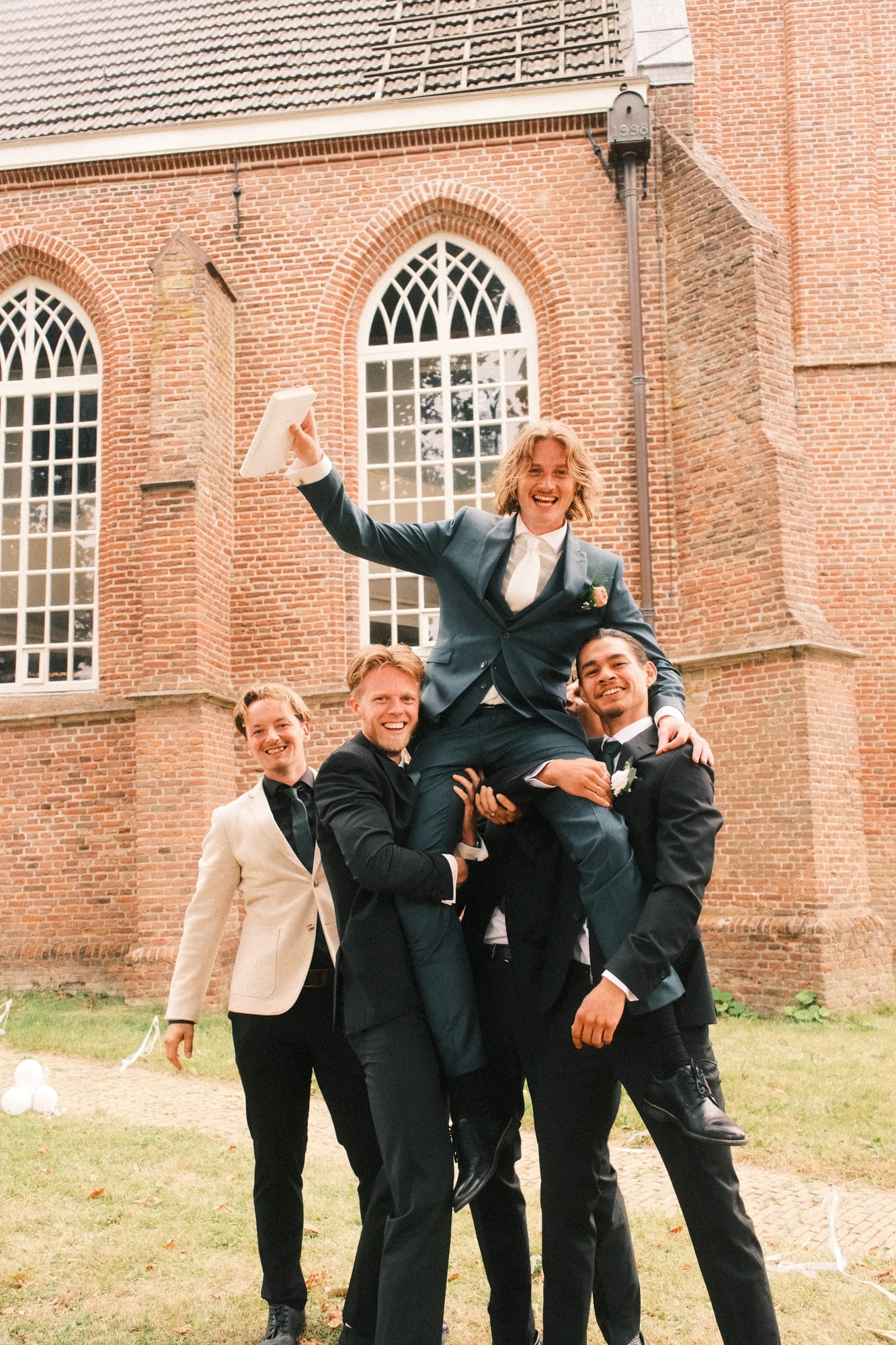 De bruidegom wordt door zijn vrienden opgetild voor de kerk